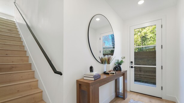 A staircase with wooden steps and a black handrail, a wooden console table with books and decorative items, a large mirror, and a door with a glass panel. - Cozy Midtown Retreat 2BR/2BA PRIVATE GARAGE (Sacramento)