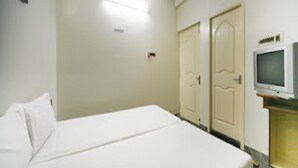 A hotel room with a bed, a television, and two doors. - La Palace (Guduvancheri)