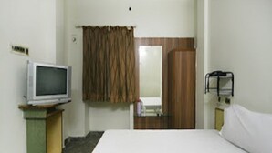 A hotel room with a bed, a television on a stand, a mirror, a door, and a small table with a bottle. - La Palace (Guduvancheri)