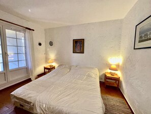 Een slaapkamer met een bed, twee nachtkastjes met lampen, een raam met gordijnen en een ingelijste foto aan de muur.