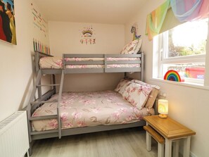 Ein Stockbett mit Blumenbettwäsche, ein kleiner Nachttisch mit Lampe und ein Fenster mit Regenbogen-Dekoration.