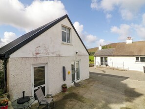 Ein zweistöckiges Haus mit geneigtem Dach, einer Haustür und einer kleinen Terrasse mit Tisch und Stühlen.