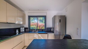 A modern kitchen with a large window, stainless steel appliances, and a black countertop. - SAINTE MAXIME Apartment with garden in residence with pool (STE MAXIME)