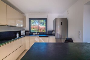 A modern kitchen with a large window, stainless steel appliances, and a black countertop. - SAINTE MAXIME Apartment with garden in residence with pool (STE MAXIME)