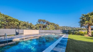A swimming pool with a tiled deck, surrounded by a fence, trees, and a grassy area. - SAINTE MAXIME Apartment with garden in residence with pool (STE MAXIME)