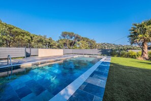 A swimming pool with a tiled deck, surrounded by a fence, trees, and a grassy area. - SAINTE MAXIME Apartment with garden in residence with pool (STE MAXIME)