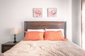 A bed with a wooden headboard, two pillows, a bedside table with a lamp, and two framed floral pictures on the wall.