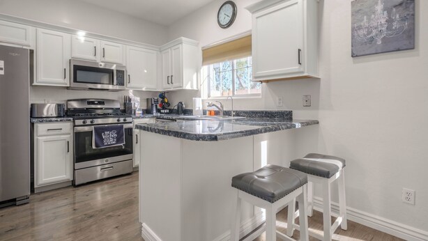 A kitchen with white cabinets, stainless steel appliances, a granite countertop, and a clock on the wall.