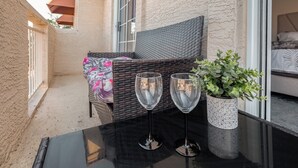 A balcony with a wicker sofa, two wine glasses, and a potted plant.