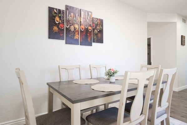 A dining area with a wooden table, six chairs, and three wall-mounted paintings.