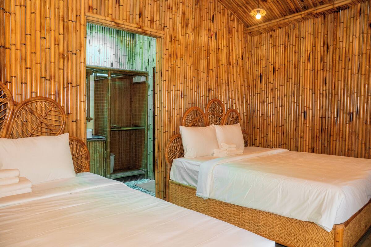 Una habitación con dos camas, paredes de bambú y techo de madera.