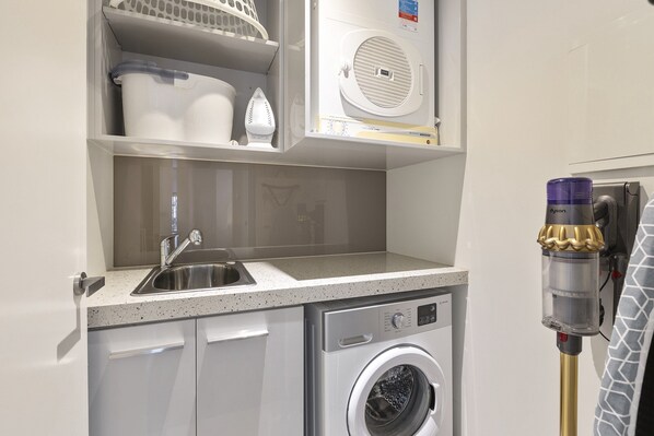 Ein kleiner Hauswirtschaftsraum mit Waschmaschine, Spüle und einem Dyson Staubsauger.