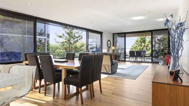 A modern interior with a dining area, a sofa, and a view of the outdoors. - Waterfront Apartment With Stunning Bay Views (Geelong)