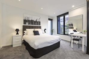 Un dormitorio moderno con una cama grande, mesitas de noche, un escritorio y un espejo.