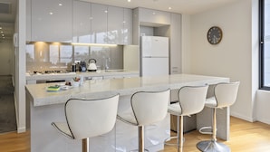 A modern kitchen with a central island, bar stools, and a refrigerator. - Waterfront Apartment With Stunning Bay Views (Geelong)