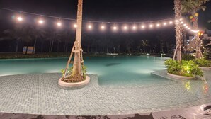 Ein Poolbereich bei Nacht mit Lichterketten, Palmen und einem gefliesten Pool.