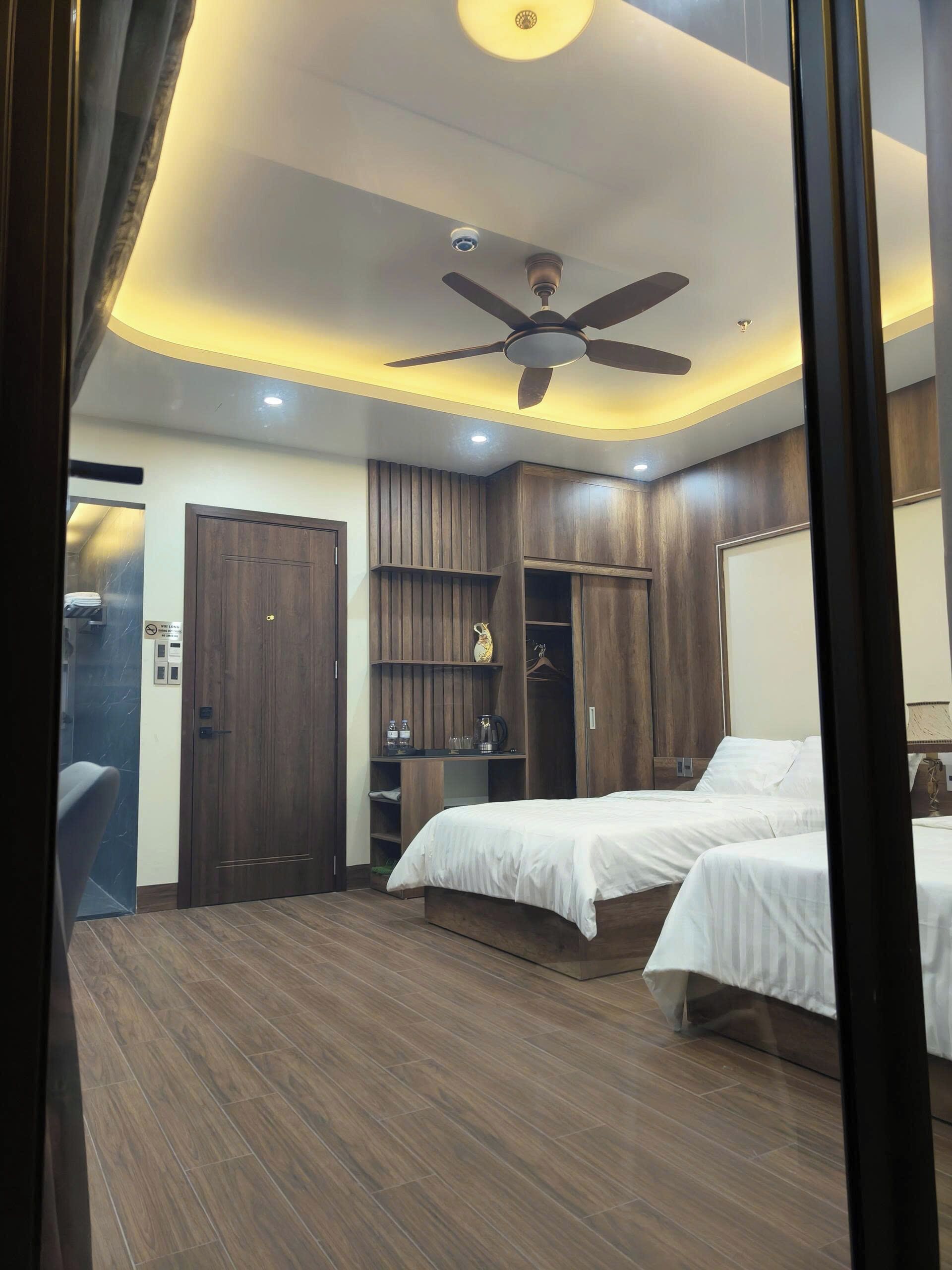 A bedroom with two beds, a ceiling fan, built-in wardrobe, and a small seating area.