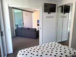 A bedroom with a bed, a TV mounted on the wall, a coat rack, and a sliding door leading to a living area. - River & fireworks visible from the balcony! (Brisbane)