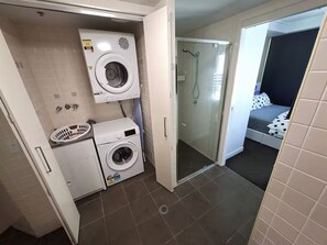 A compact bathroom with a washing machine, a dryer, and a glass shower enclosure. - River & fireworks visible from the balcony! (Brisbane)
