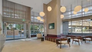 Un vestíbulo amplio con techo alto, ventanas grandes y una zona de estar con mobiliario de madera.
