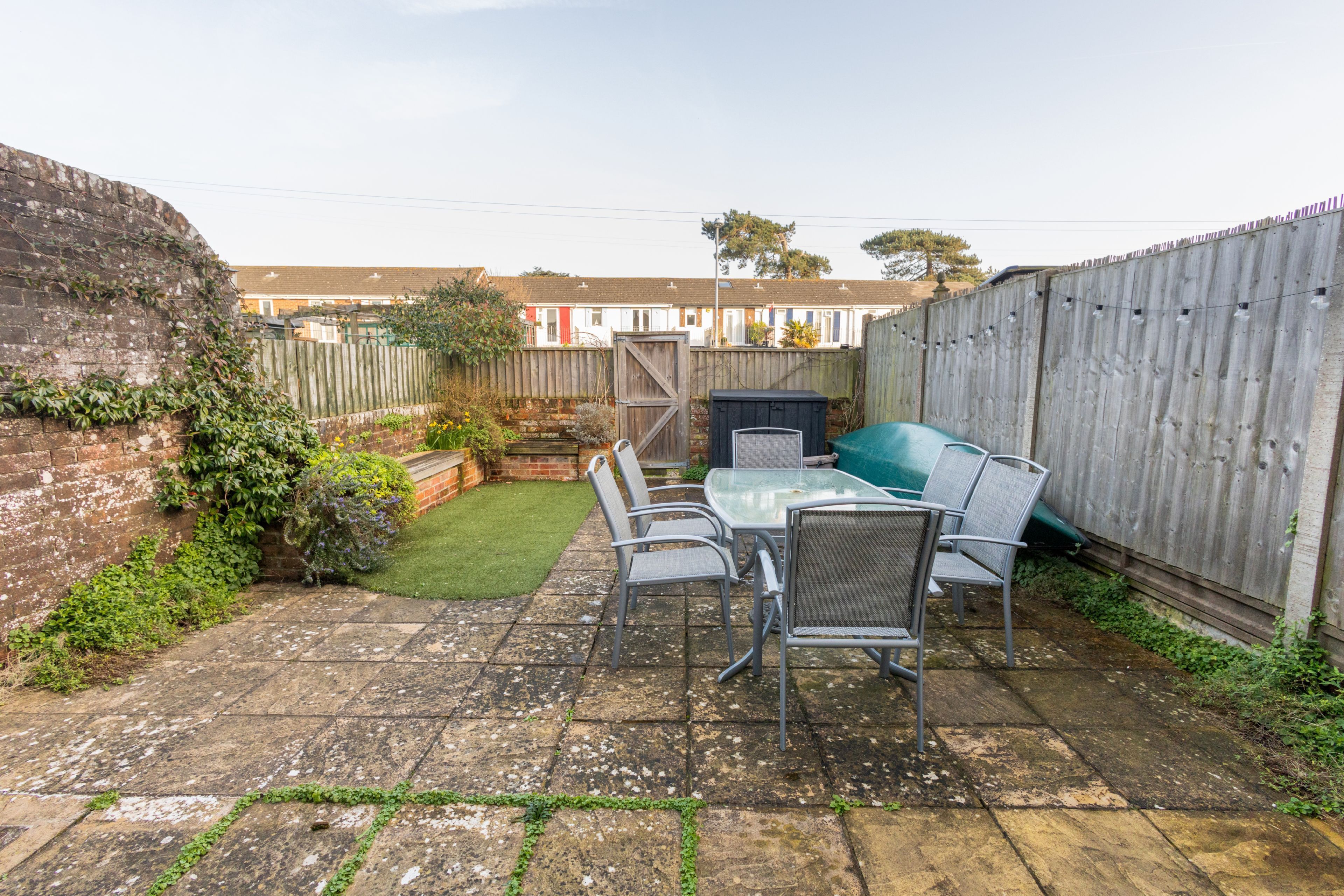 A patio with a table and chairs, a small lawn, and a wooden fence.