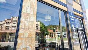 Un bâtiment doté de grandes fenêtres, une enseigne indiquant qu’un bistro est ouvert sept jours sur sept, et le reflet de l’environnement.