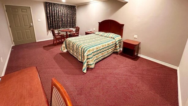 Um quarto com cama, escrivaninha, cadeira e uma pequena mesa.