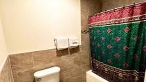 Casa de banho com sanita, chuveiro com cortina estampada e um porta-toalhas.