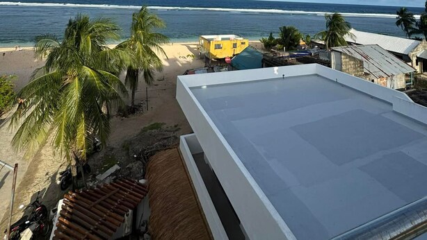 Vista a la playa con un edificio blanco, palmeras y cielo despejado.