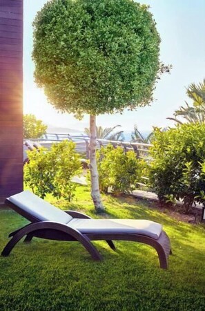 Ein gepflegter Rasen mit einem außergewöhnlichen kugelförmigen Baum, einer Liege und Blick auf den Ozean.