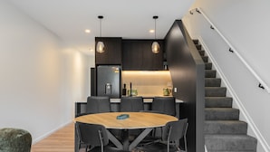 Una cocina moderna con armarios oscuros, una mesa de comedor de madera y una escalera con peldaños alfombrados de color gris.