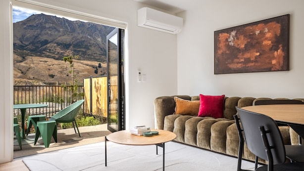Una sala de estar con sofá, una mesa de centro y una mesa de comedor. Se ve una vista de montañas a través de una puerta de vidrio.