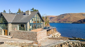 Un bâtiment en pierre doté de grandes fenêtres et d’un balcon donnant sur un lac.