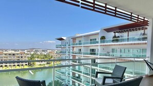 A balcony with wicker chairs, a view of a body of water, and a multi-story building in the background. - Near the beach, with a terrace and beautiful views (Mazatlán)