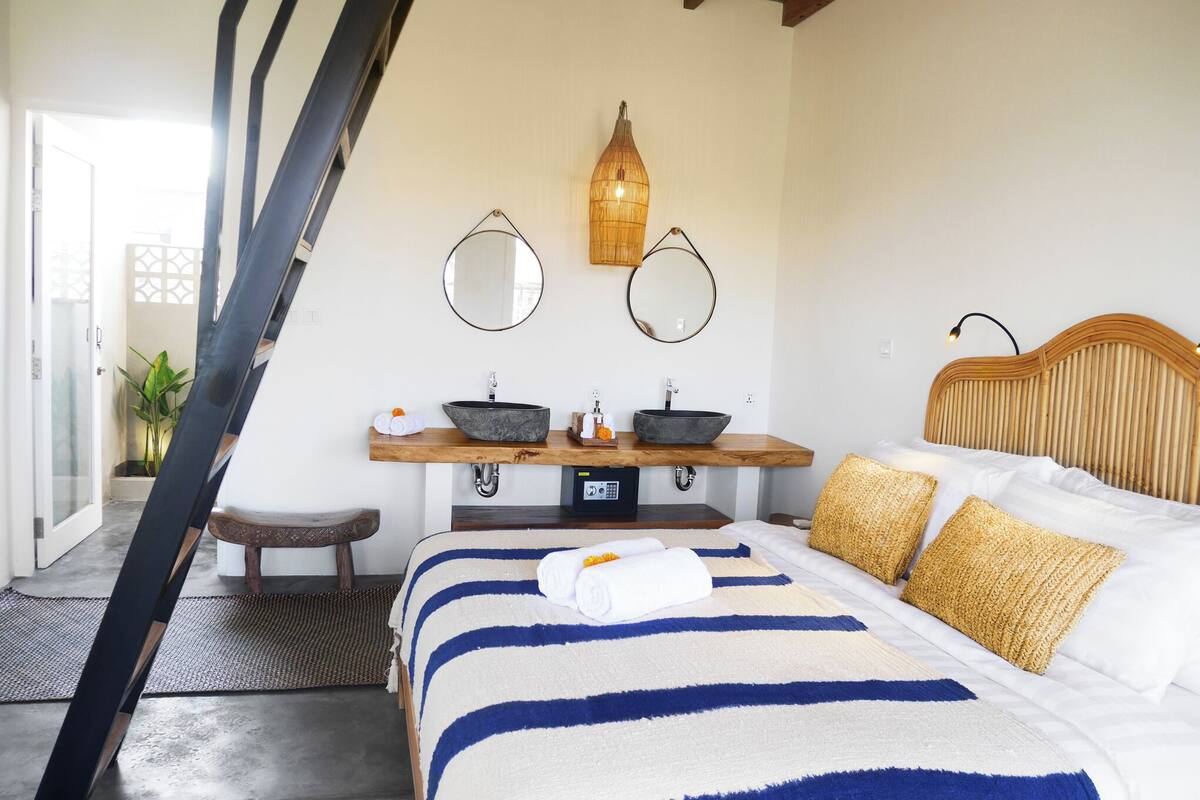 Ein Schlafzimmer mit einem Bett, zwei Nachttischen, einem Spiegel, einer Hängeleuchte und einem Holzkopfstück.