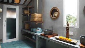 A kitchen with a hanging basket, a wooden shelf, a stone basin, and a window with a view. - AMAR Beach Boutique Hotel (Pererenan)
