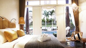Camera d'albergo con un letto, due cuscini, una lampada da comodino, una sedia e vista su una piscina e palme.
