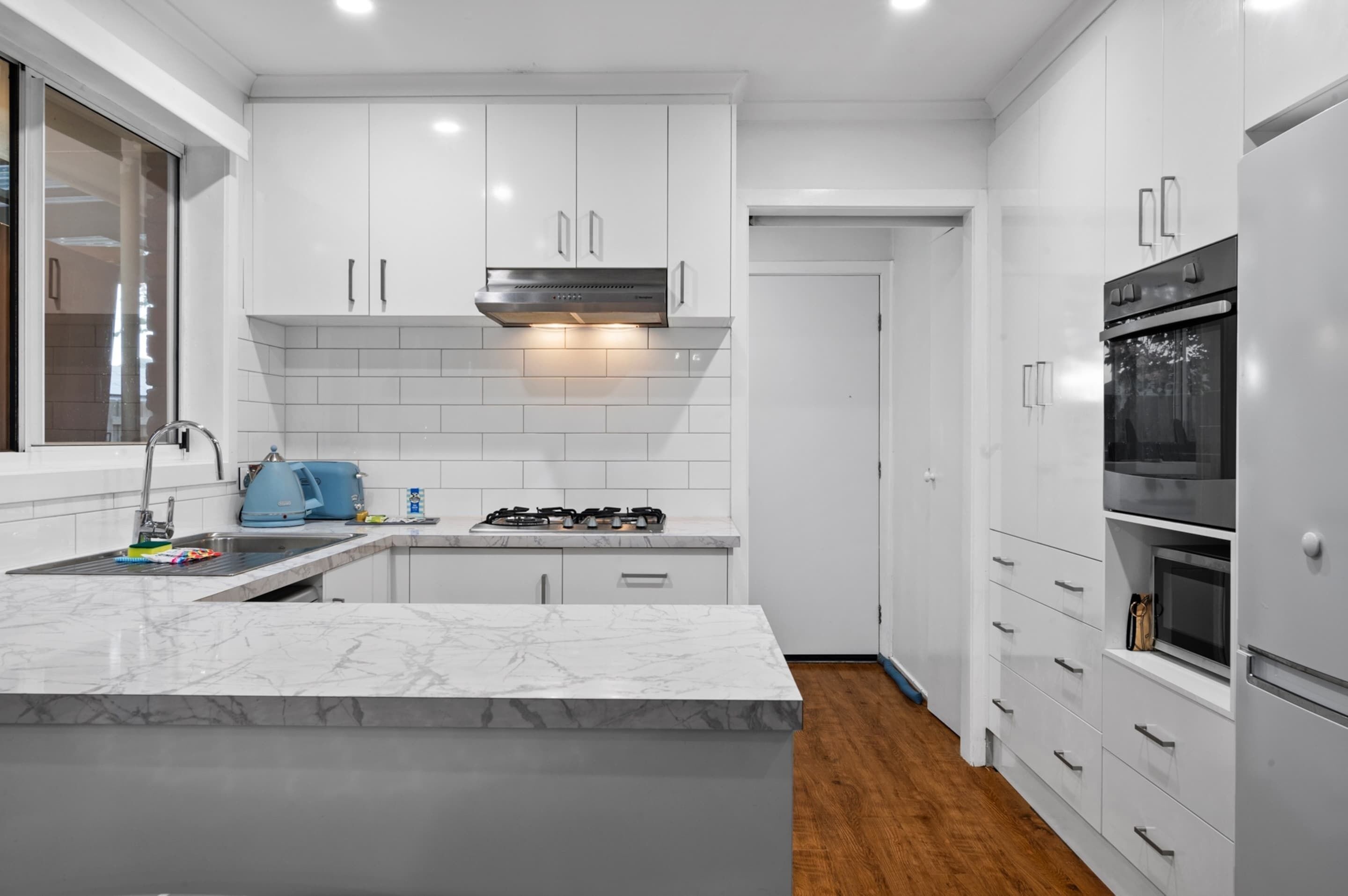 A modern kitchen with white cabinets, a marble countertop, a gas stove, and a built-in oven.