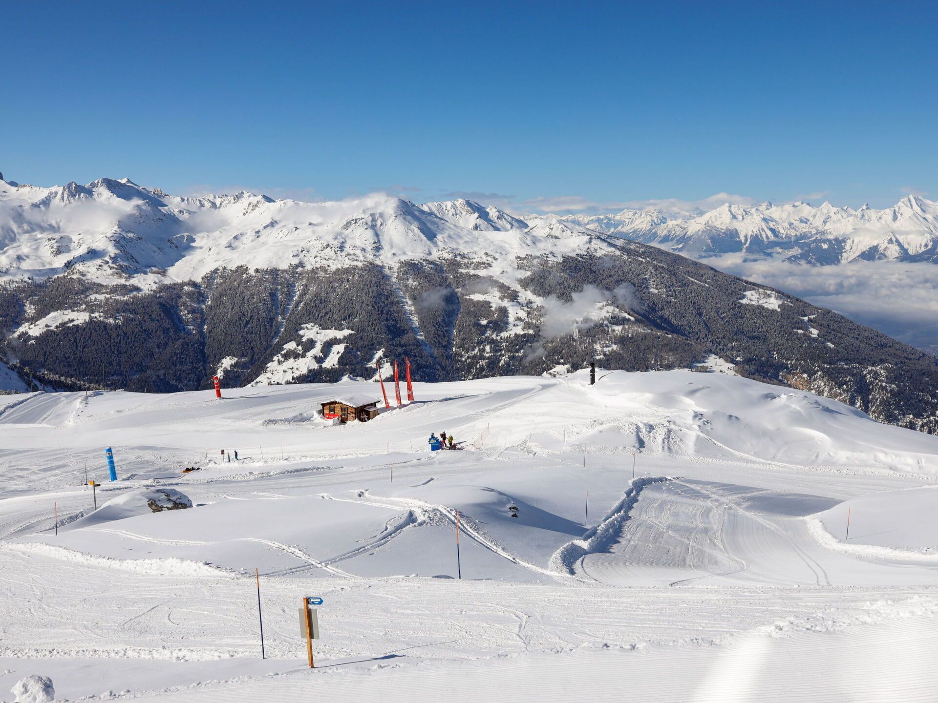 A snow-covered ski slope with marked trails and a small lodge in the background.