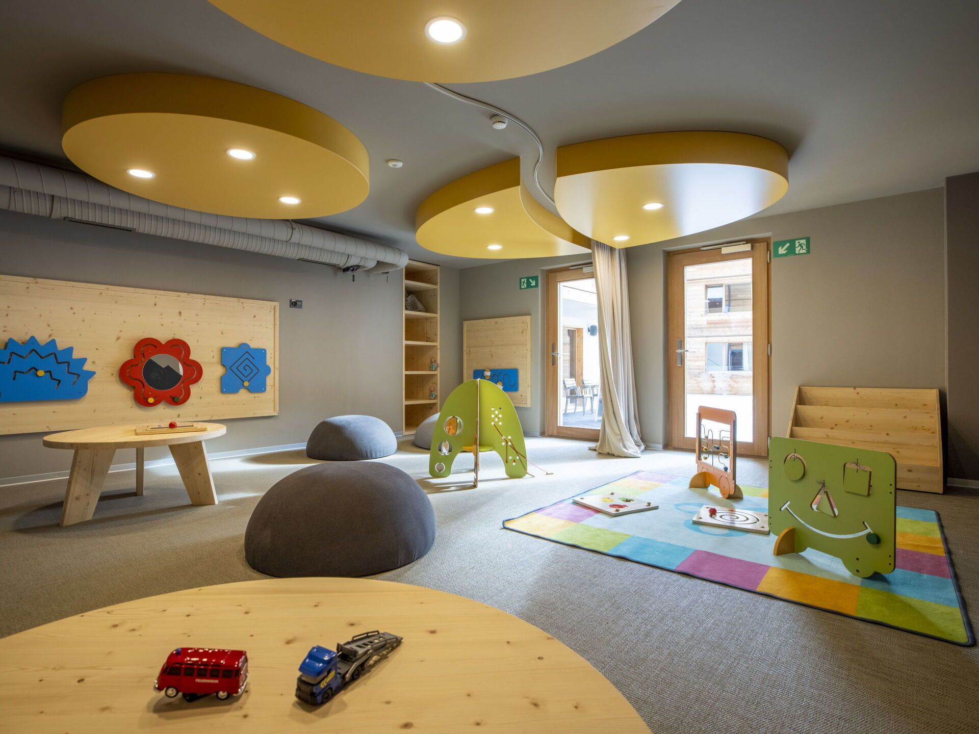 A children's playroom with a wooden table, bean bags, and a colorful play mat.