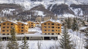 Eine Gruppe Holzhäuser mit einer Skipiste im Hintergrund.