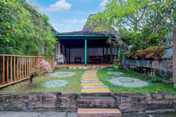 A covered outdoor seating area with a stone pathway, surrounded by greenery and plants. - Hotel O near Parangtritis Beach formerly (Parangtritis)