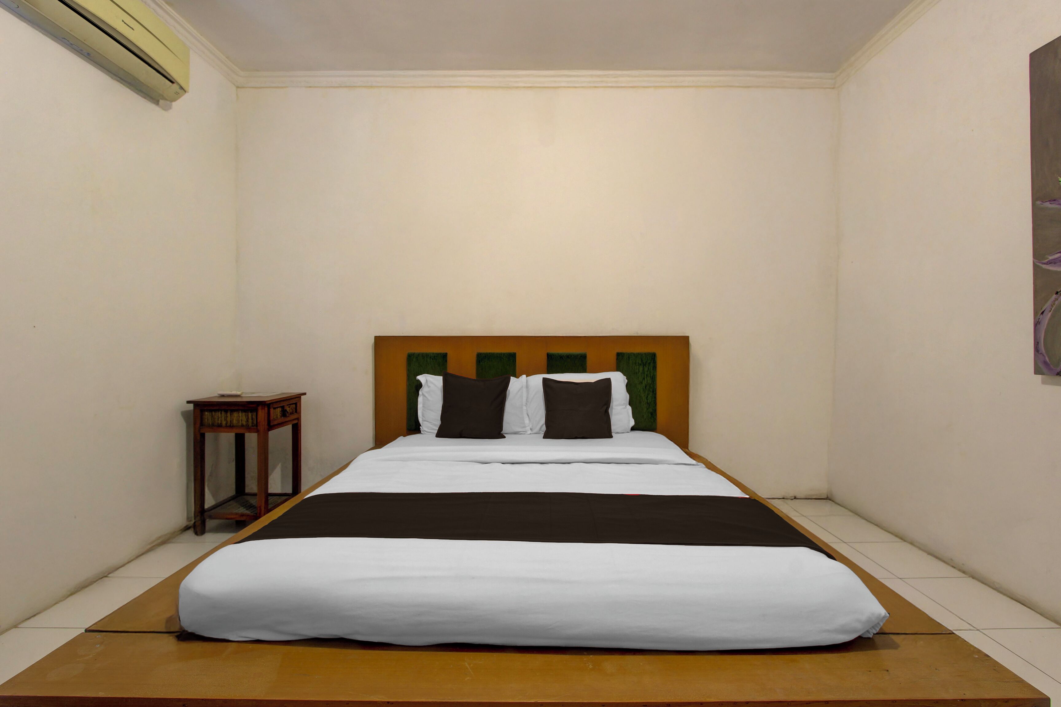 A single bed with a wooden headboard, white bedding, and a small bedside table with a lamp.