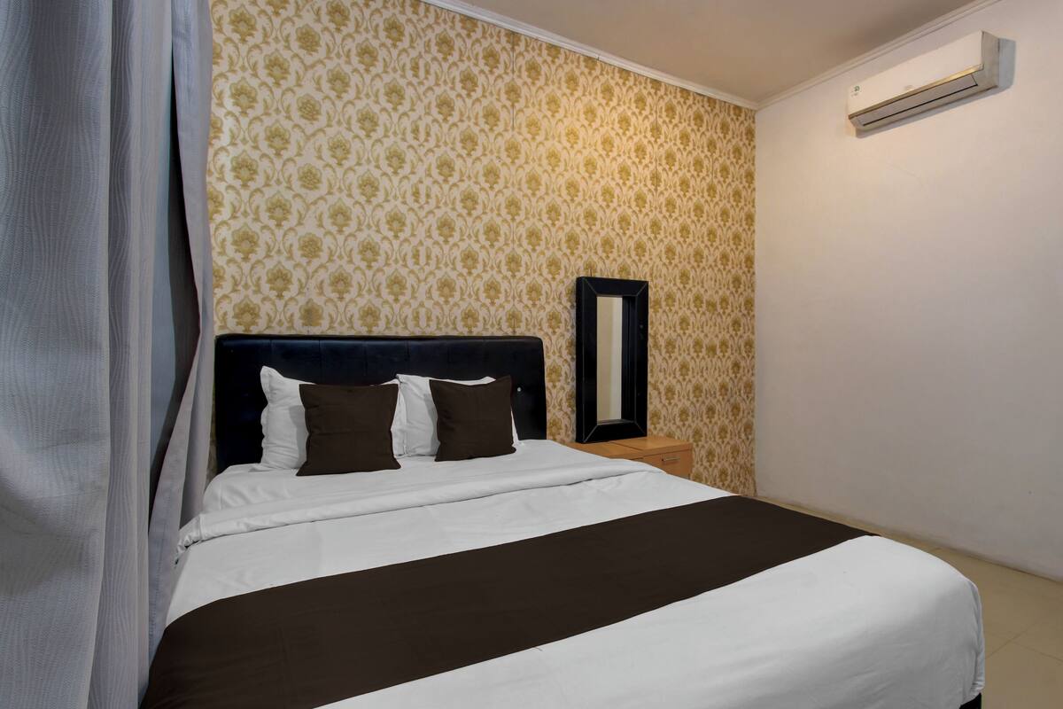 Una cama bien hecha con cabecera, una mesita de noche, un espejo y un aire acondicionado de pared.
