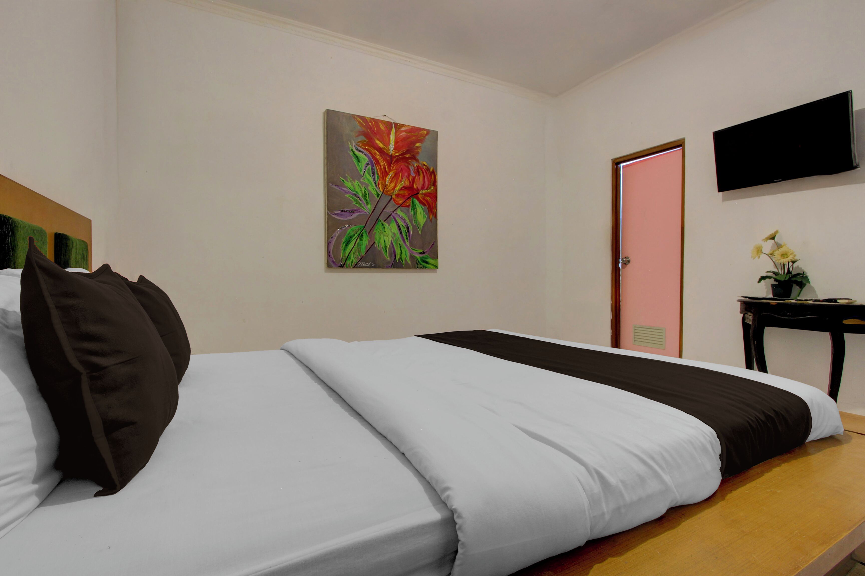 Una habitació d'hotel amb un llit, un quadre a la paret, una televisió i una porta.