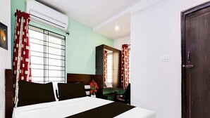 Una habitación de hotel con cama, armario, escritorio y ventana con cortinas.