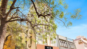 Un hotel con un letrero, un árbol en primer plano y un edificio con balcón.