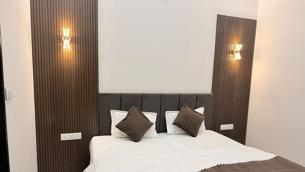 A bedroom with a bed, pillows, a headboard, and wall-mounted lights. - Kiwi Inn Hotel Palda (Indore)