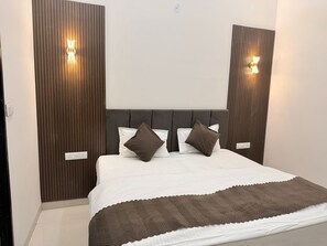 A bedroom with a bed, pillows, a headboard, and wall-mounted lights. - Kiwi Inn Hotel Palda (Indore)