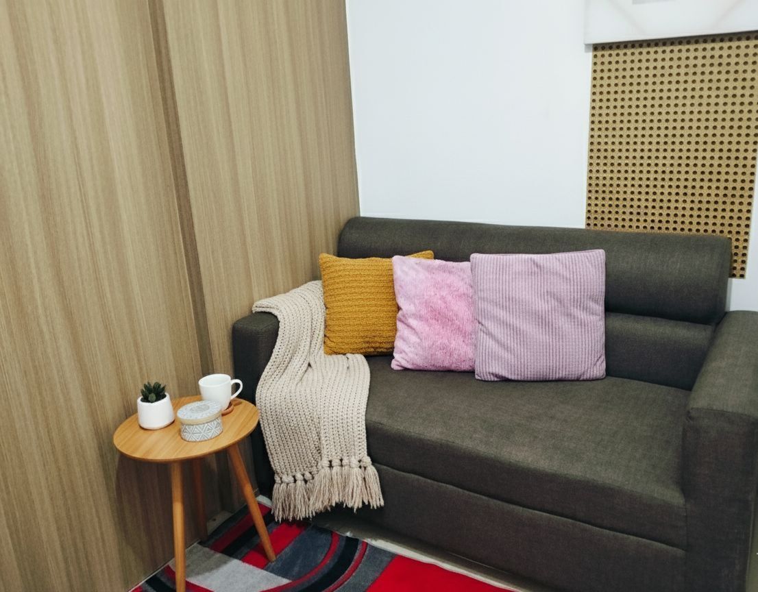 Ett modernt vardagsrum med en grå soffa, ett litet runt sidobord i trä, en röd och svart randig matta och en väggmonterad akustikpanel.